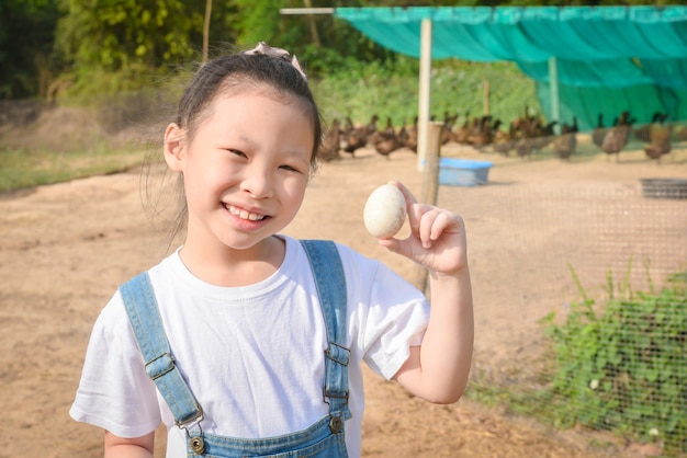 写真 彼女の農場からアヒルの卵を見せて微笑む小さなアジアの女の子。