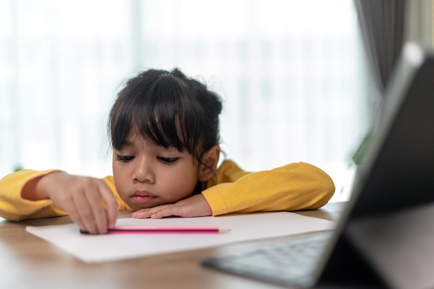 Little Asian girl sitting alone and looking out with a bored face Preschool child laying head down on the table with sad bored with homework spoiled child