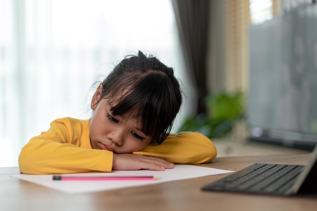 Little Asian girl sitting alone and looking out with a bored face Preschool child laying head down on the table with sad bored with homework spoiled child