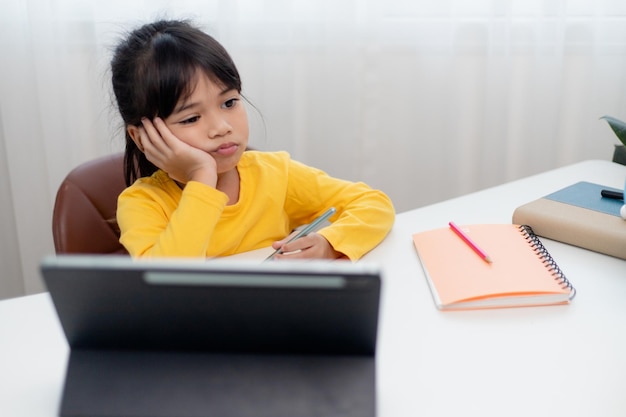 Little Asian girl sitting alone and looking out with a bored face Preschool child laying head down on the table with sad bored with homework spoiled child