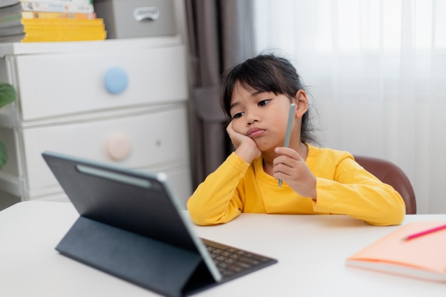 Little Asian girl sitting alone and looking out with a bored face Preschool child laying head down on the table with sad bored with homework spoiled child