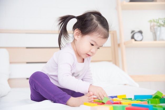 Little asian girl sitting on bed and playing toys at home