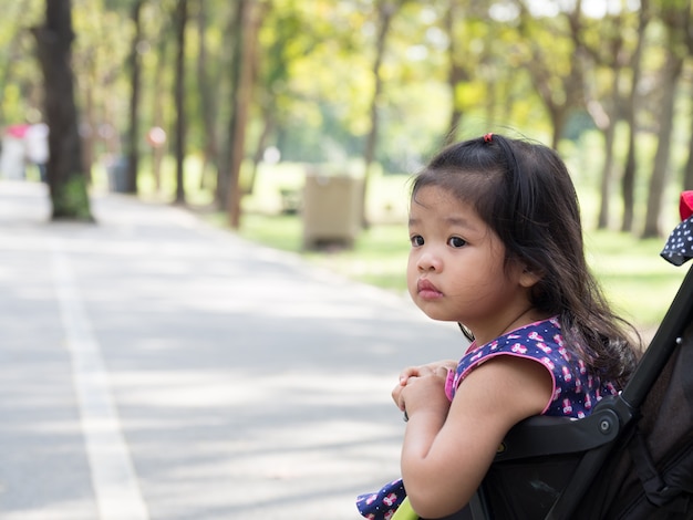 Piccola ragazza asiatica che si siede in un passeggiatore al parco pubblico.