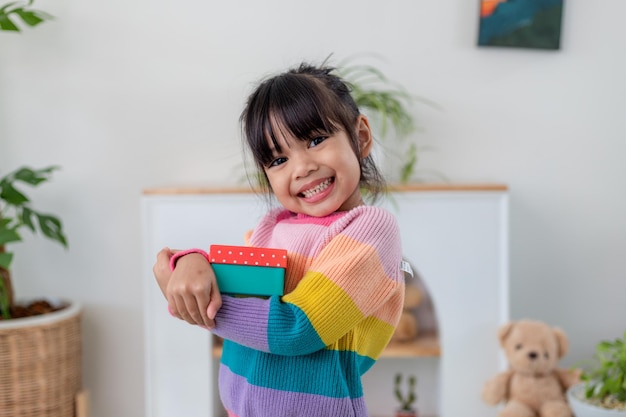 Little Asian girl smile and excited and holding red gift box in living room background. child holding gift box in Christmas and New year.Asian child girl smile and surprise.