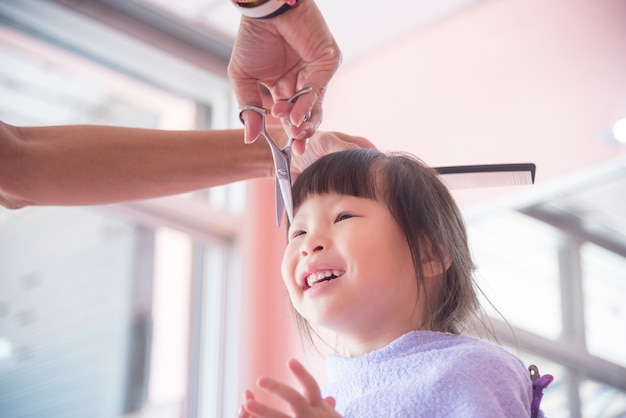 Little asian girl smiling while hairdresser cutting her hair