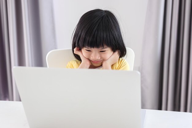 小さなアジアの女の子の学生は、自宅でラップトップコンピューターを使用してオンラインで勉強します