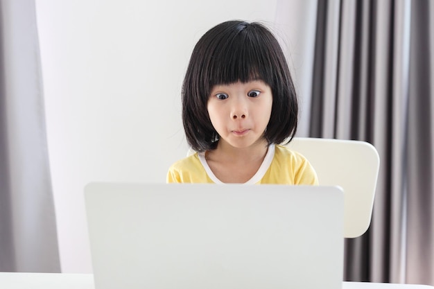 小さなアジアの女の子の学生は、自宅でラップトップコンピューターを使用してオンラインで勉強します