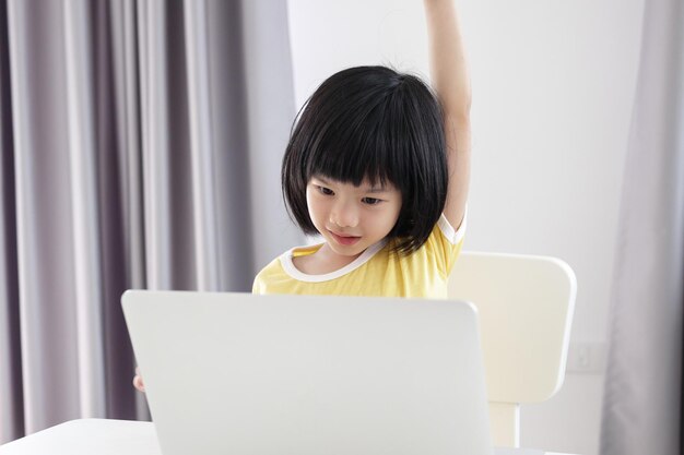 小さなアジアの女の子の学生は、自宅でラップトップコンピューターを使用してオンラインで勉強します