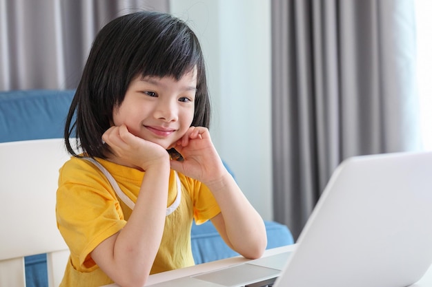 La piccola studentessa asiatica studia online utilizzando il computer portatile a casa