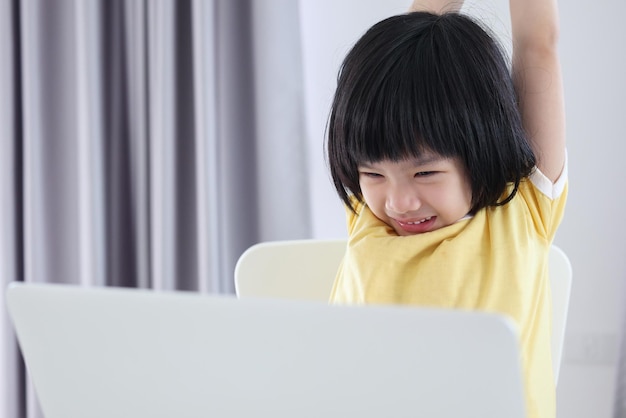 La piccola studentessa asiatica studia online utilizzando il computer portatile a casa