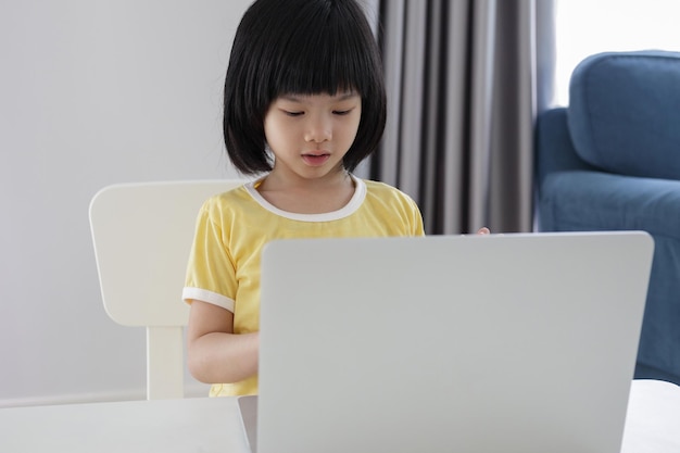 小さなアジアの女の子の学生は、自宅でラップトップコンピューターを使用してオンラインで勉強します