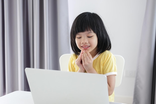 Маленькая азиатская студентка учится онлайн, используя портативный компьютер дома