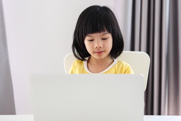 小さなアジアの女の子の学生は、自宅でラップトップコンピューターを使用してオンラインで勉強します