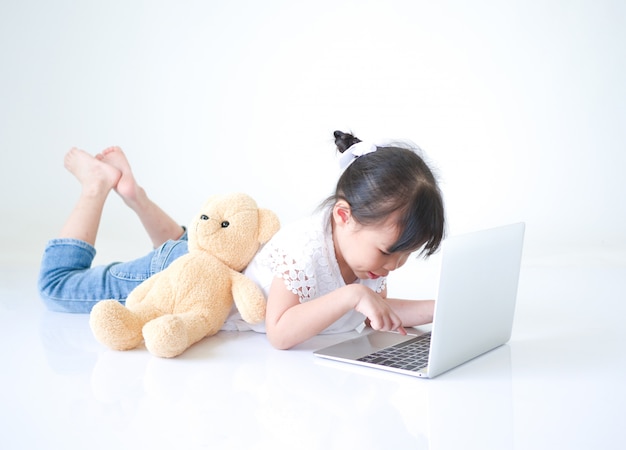 Little Asian girl typing message on laptop over white background.