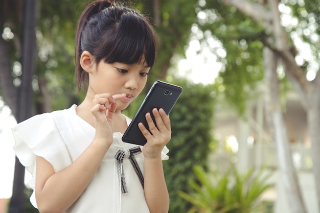 カフェでスマートフォンを使用している小さなアジアの女の子。自然光のアウトドアライフスタイル。