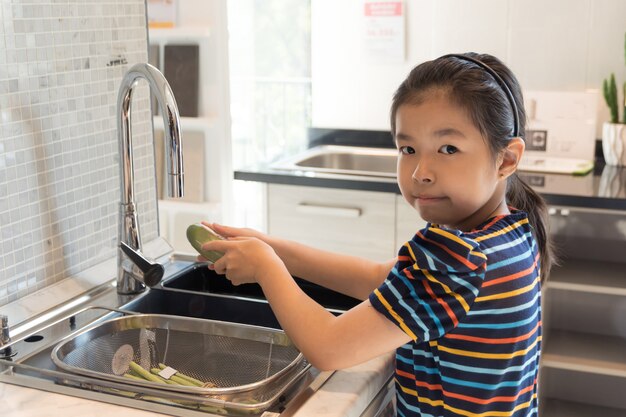 小さなアジアの女の子は野菜を洗う