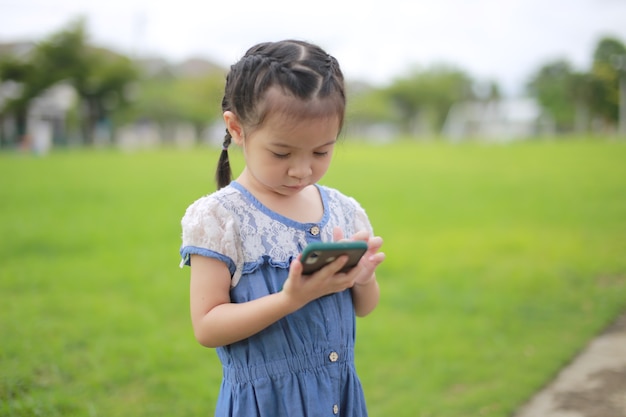 屋外のスマートフォンを持つ小さなアジアの女の子。