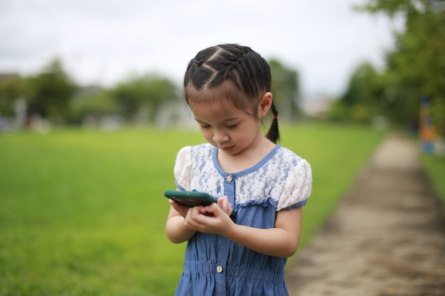 屋外のスマートフォンを持つ小さなアジアの女の子。