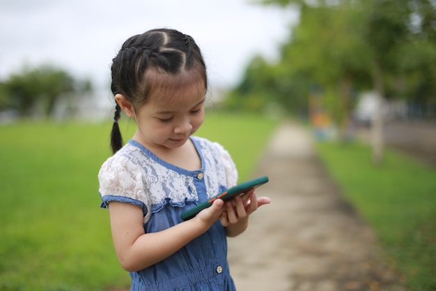 Piccola ragazza asiatica con uno smartphone all'aperto.