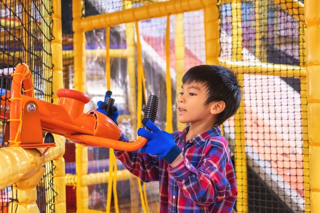 Piccolo bambino asiatico si diverte a giocare con il cannone palla nel parco giochi al coperto