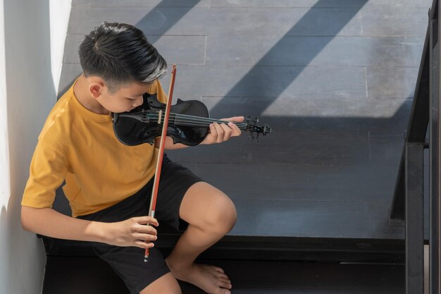 A Little Asian kid playing and practice violin musical string instrument against in home