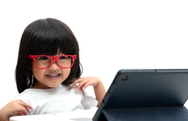 Little Asian Preschooler girl wearing red glasses and using tablet pc on white background, Asian girl talking and learning with a video call with a tablet, Educational concept for school kids.