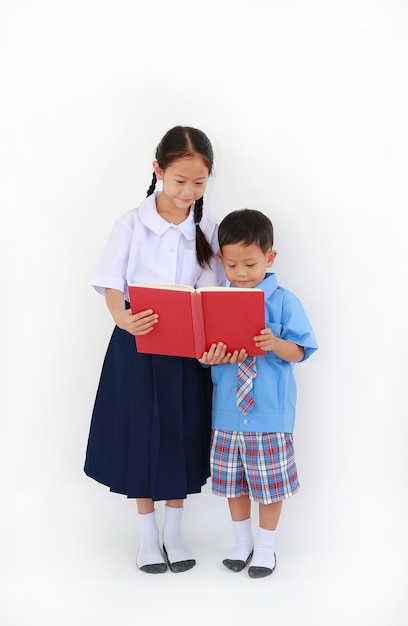小さなアジアの学校の男の子と女の子は、タイの学校の制服を着て、白い背景で隔離の本を読んで立っています。全長