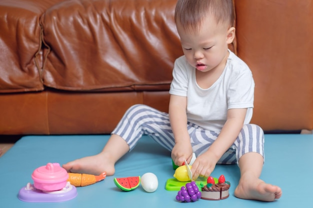 작은 아시아 유아 소년 아이는 집에서 바닥에 앉아 요리 장난감을 가지고 혼자 놀고 있습니다.