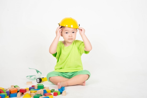 나무 블록을 착용하는 작은 아시아 유아 소년 헬멧 엔지니어를 착용