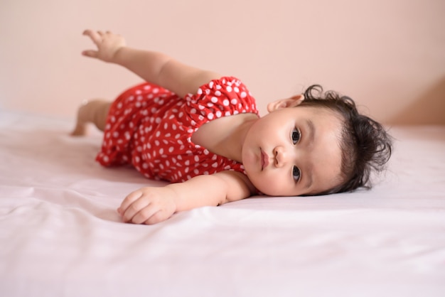 Little Asian wavy black hair baby, a cute toddler dressed in red lying on the bed and look at camera