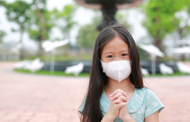 Little asian young girl child wear face mask pray gesture for stop covid-19 during coronavirus outbreak in thailand