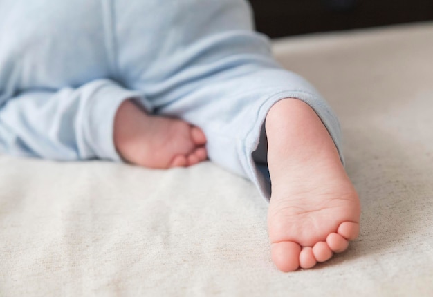 Little baby in blue pants crawling on the bed and his small foot close-up