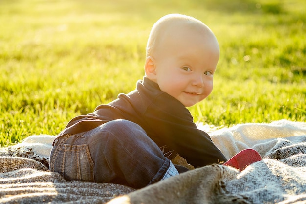 Little baby boy on a blanket in the park in summer.