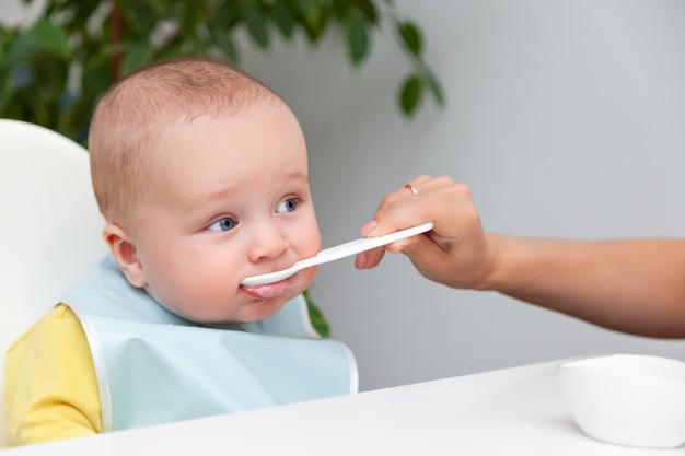 Маленький мальчик в цветной одежде ест йогурт из ложки, грязный рот
