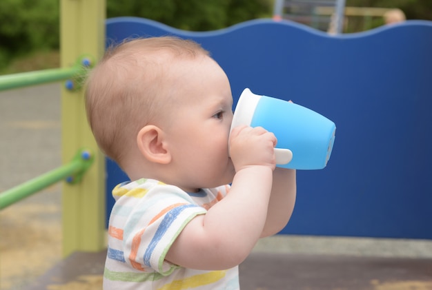 小さな男の子はプラスチック製のマグから水を飲む