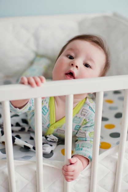 Little baby boy lying in his crib in light room and play with his toys