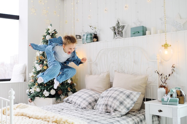 パジャマ姿の小さな男の子は幸せでベッドにジャンプします