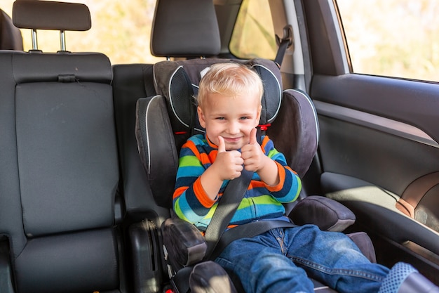 Little baby boy sitting on a car seat buckled up with his thumb up in the car.