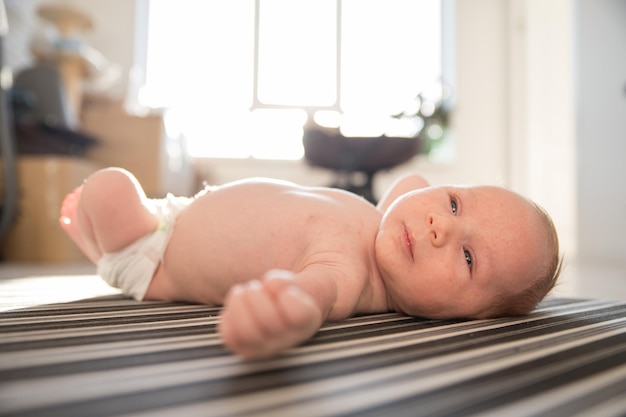 A little baby in a diaper restlessly lying on his back on striped sheets in day light