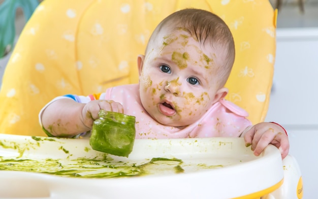 Little baby eats broccoli puree himself. Selective focus. People.