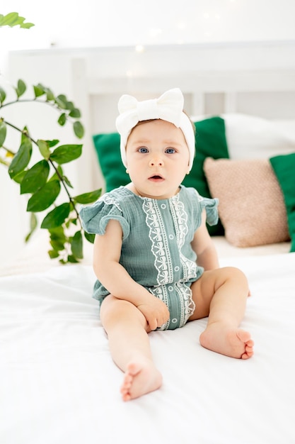 Little baby girl on the bed at home in a green bodysuit smiling or laughing cute funny baby at home before going to bed lifestyle