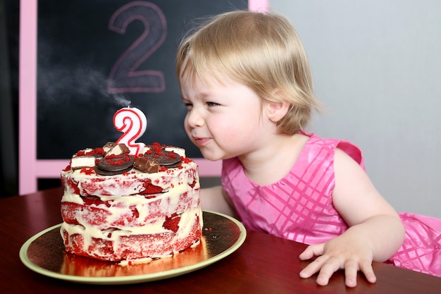 小さな女の赤ちゃんがケーキにろうそくを吹き消します。 2歳の誕生日