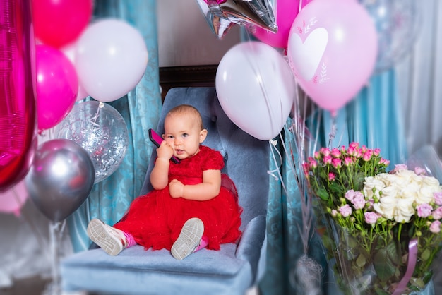 Piccola neonata che celebra il suo primo compleanno seduto su una sedia in un vestito rosso