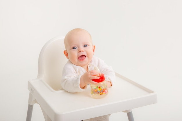 La piccola neonata beve l'acqua da una bottiglia all'interno si siede su un seggiolone