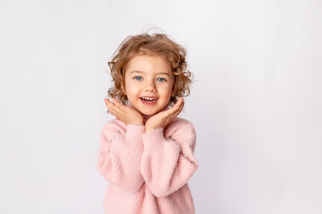 Фото Маленькая девочка в розовой зимней одежде на белом фоне радуется, место для текста