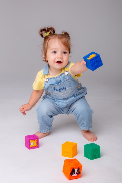 小さな女の赤ちゃんは白い背景の上に座って、カラフルなキューブ子供の遊びおもちゃキューブで遊んでいます。