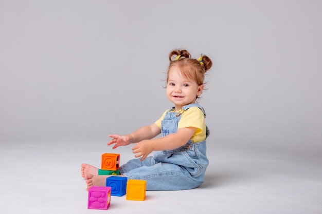 little baby girl is sitting on a white background and playing with colorful cubes. kid's play toy