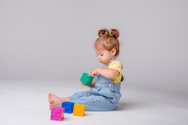 어린 소녀는 흰색 배경에 있고 다채로운 큐브 아이의 놀이 장난감 큐브를 가지고 노는