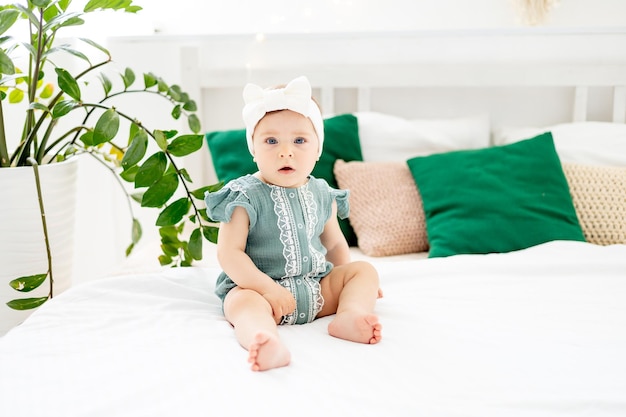 사진 초록색 바디슈트를 입은 어린 소녀가 집에서 침대에 앉아 미소 짓거나 웃는 귀여운 재미있는 아기가 집에서 잠자리에 들기 전에 생활 방식