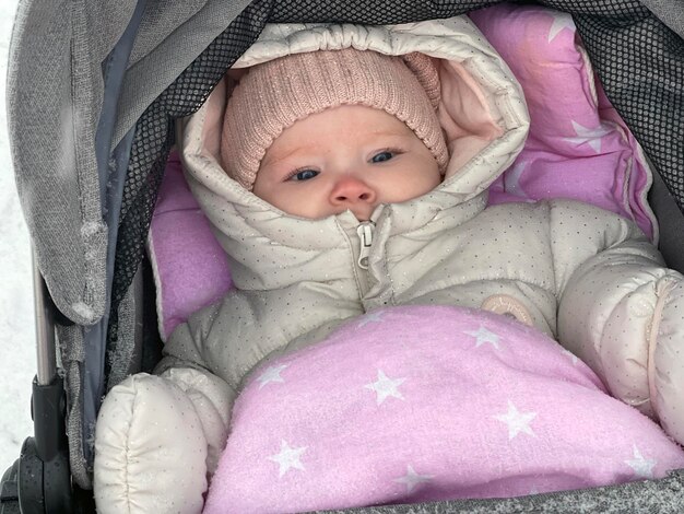 Little baby girl in the pram on a snowy winter day